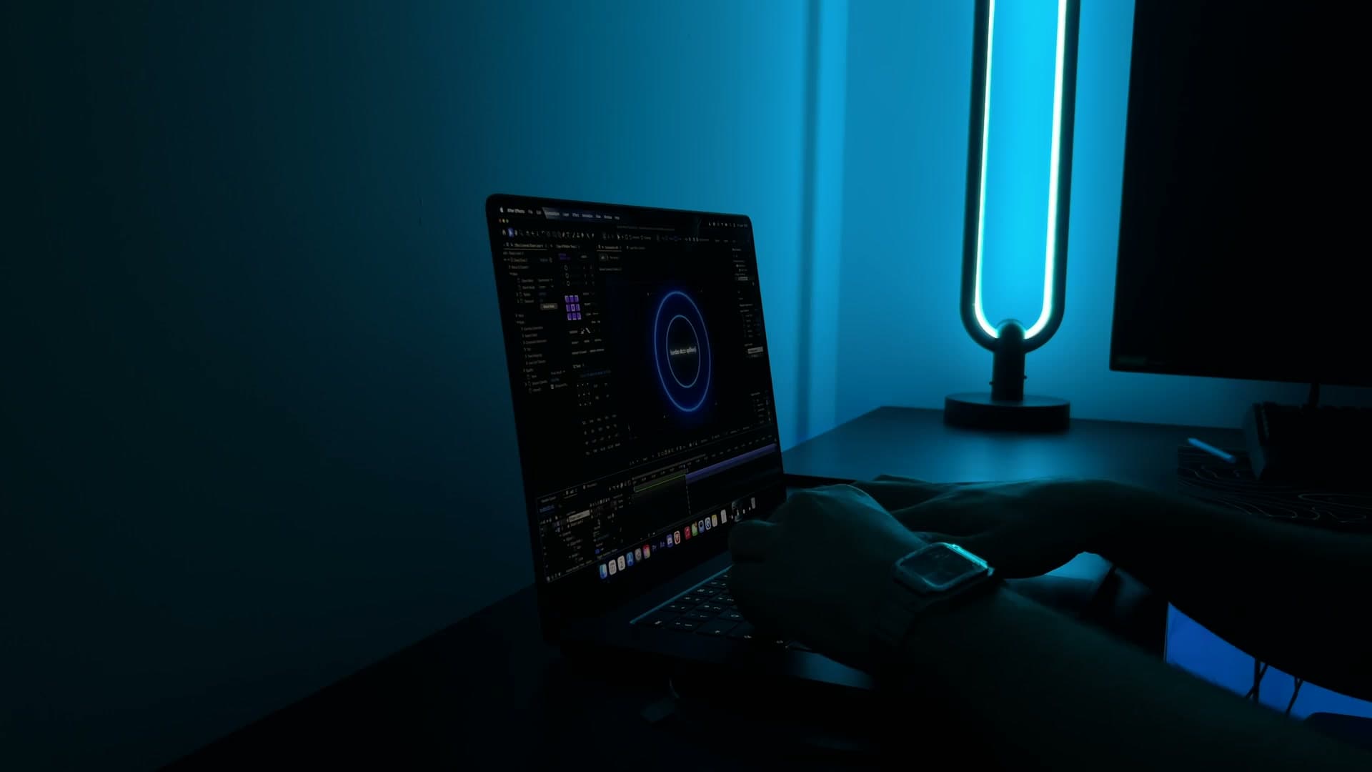 Biurko montażysty nocą: laptop z otwartym After Effects, niebieski neon i dłonie na klawiaturze